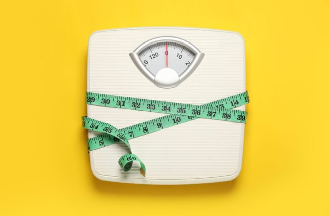 Weigh,Scales,Tied,With,Measuring,Tape,On,Yellow,Background,,Top